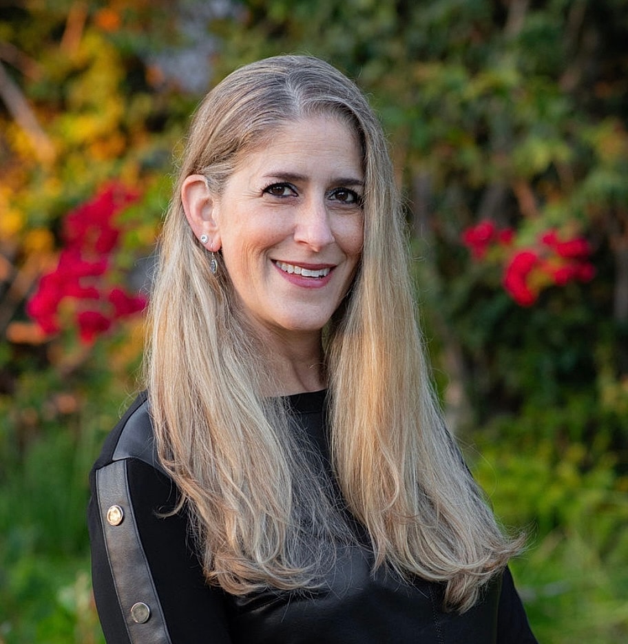 Smiling woman wearing a white coat and earrings.