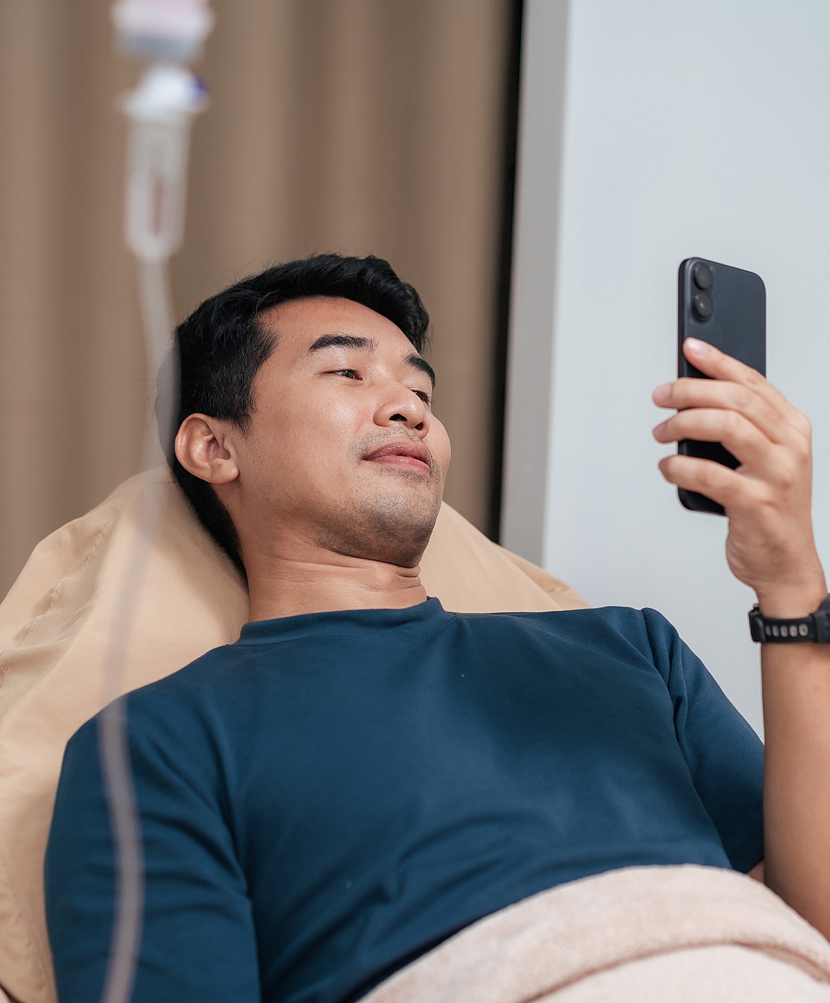 Torrance IV therapy man in bed using smartphone, IV drip nearby.