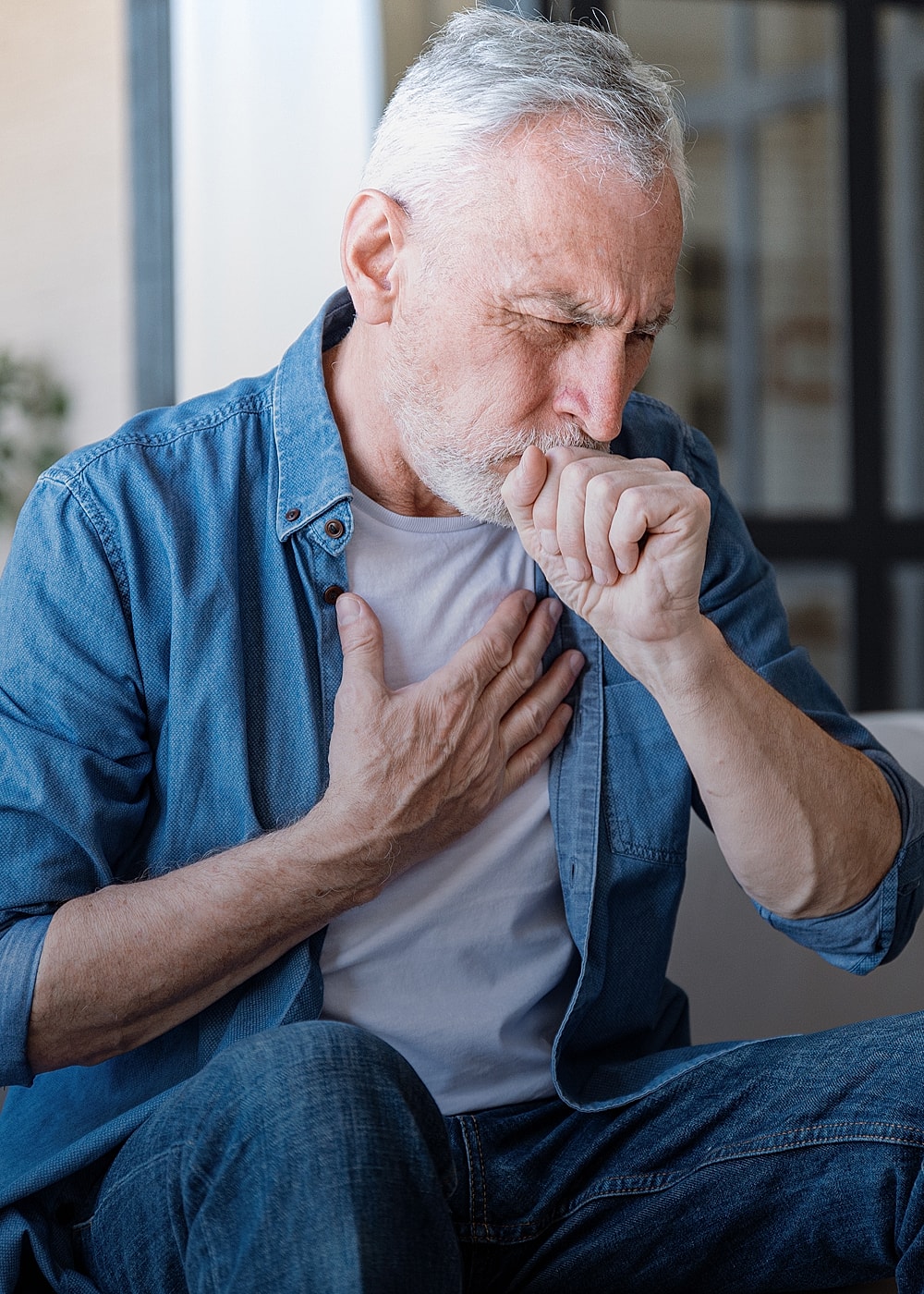 Elderly man coughing and holding his chest.